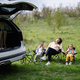 Mother with two daughters sit on chair against car open trunk on picnic. - PhotoDune Item for Sale