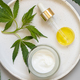 Cream jar and pipette near green cannabis leaves on grey table. Cosmetic Mockup - PhotoDune Item for Sale