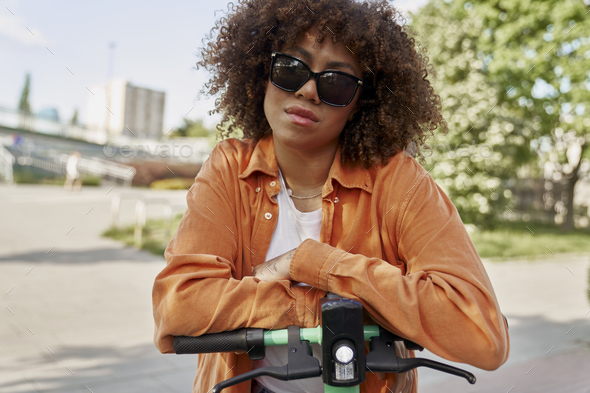 Front view of black woman in sunglasses riding an electric scooter - Stock Photo - Images