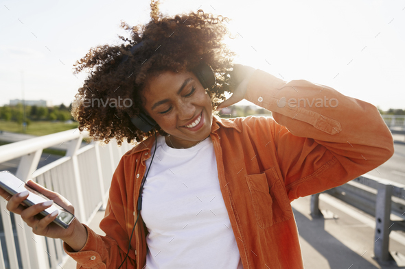 Black woman wearing headphones and dancing on the bridge - Stock Photo - Images