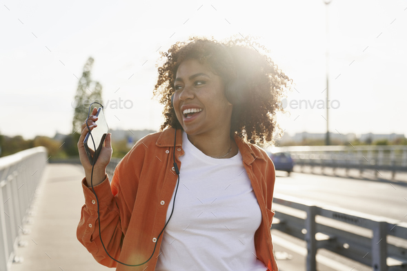 Cheerful black woman wearing headphones and dancing on the bridge - Stock Photo - Images