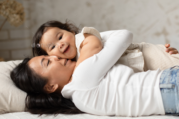 Chinese Mother Embracing Her Child Daughter Lying In Cozy Bedroom - Stock Photo - Images