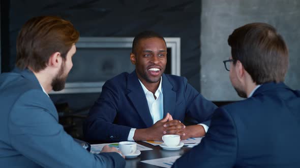 Happy african american man in suit with colleagues at the table at meeting alt