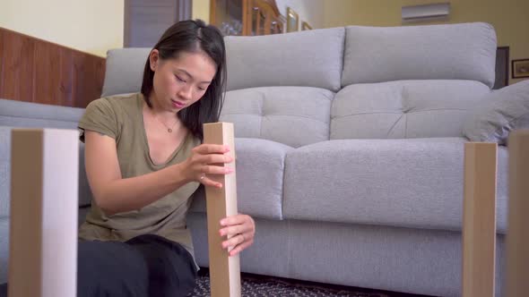 Asian woman assembling table in living room alt