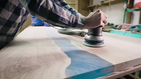 The Carpenter Processes the Surface of a Wooden Tabletop with a Grinder alt