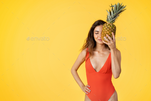Happy millennial mixed race lady in swimsuit hold pineapple, has fun, enjoy fruit - Stock Photo - Images
