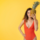 Happy millennial mixed race lady in swimsuit hold pineapple, has fun, enjoy fruit - PhotoDune Item for Sale