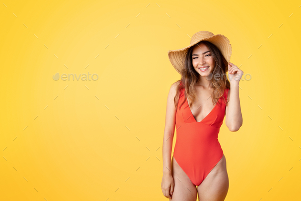 Happy millennial mixed race lady in swimsuit and hat enjoy rest, vacation, isolated on yellow studio - Stock Photo - Images