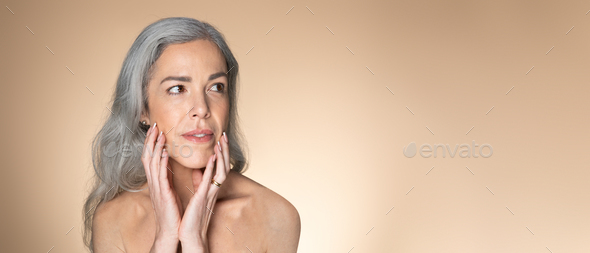 Reflections of time. Grey-haired senior woman touching her glowing face skin and looking aside at - Stock Photo - Images