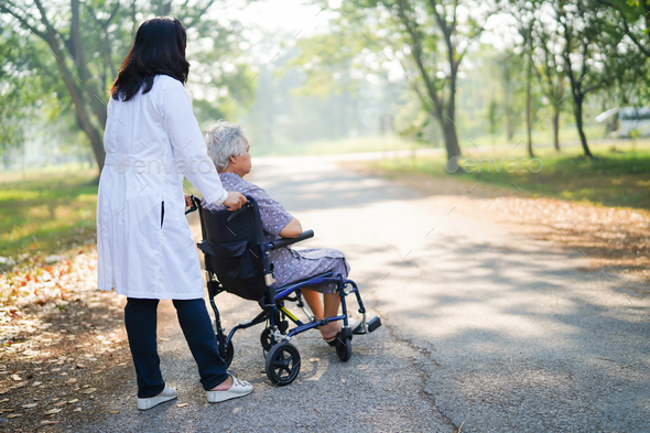 Doctor help and care Asian senior woman patient sitting on wheelchair at park. - Stock Photo - Images