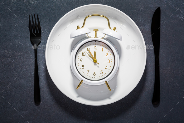 White plate and clock on a dark background with copy space.  - Stock Photo - Images