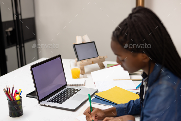 African american teenager girl doing homework, using laptop and tablet with copy space - Stock Photo - Images