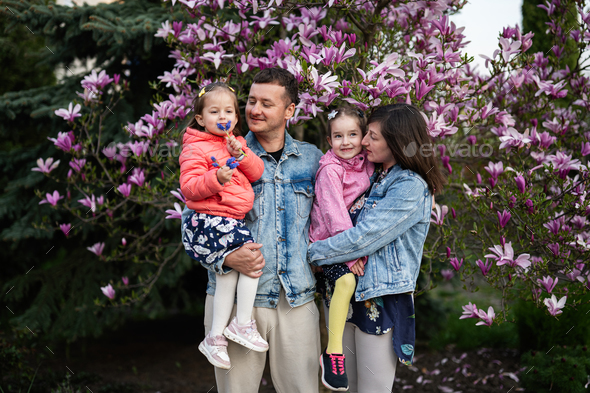 Happy family with two daughters enjoying nice spring day near magnolia blooming tree. - Stock Photo - Images