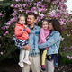 Happy family with two daughters enjoying nice spring day near magnolia blooming tree. - PhotoDune Item for Sale