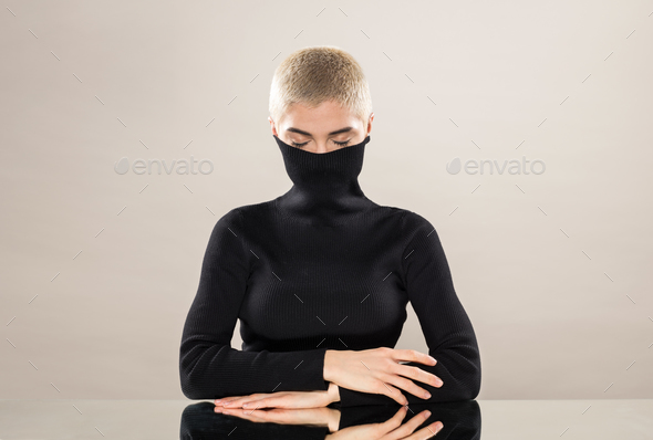 Young woman with closed eyes covering mouth with collar in studio - Stock Photo - Images