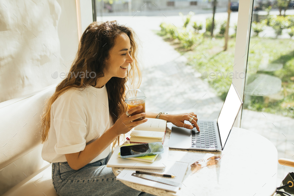 Young woman freelancer working in a coffeehouse, using her laptop and smartphone. - Stock Photo - Images