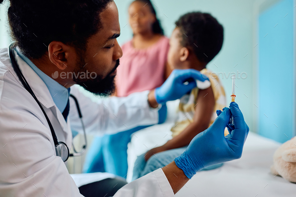 Black pediatrician giving vaccine to a child at doctor's office. - Stock Photo - Images