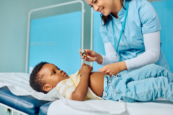 Happy nurse putting ECG electrode on black boy's chest during medical examination at the clinic. - Stock Photo - Images