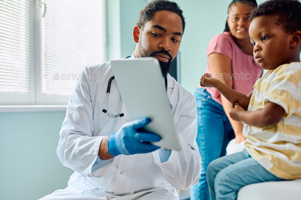 Black pediatrician and small boy using digital tablet at doctor's office. - Stock Photo - Images
