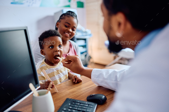Small black boy having throat exam while being with his mother at pediatrician\'s.