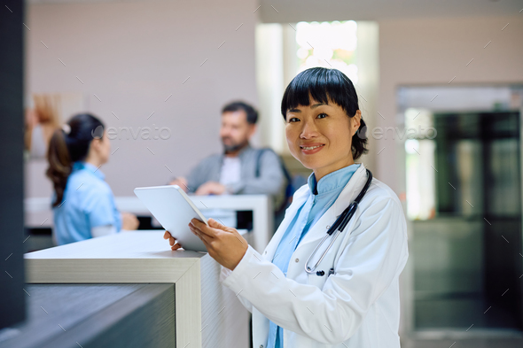 Happy Japanese doctor working on touchpad at the clinic and looking at camera. - Stock Photo - Images