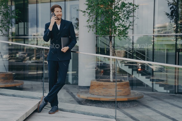 ?onfident man lawyer in dark blue suit speaks on smartphone with smile while standing outside - Stock Photo - Images