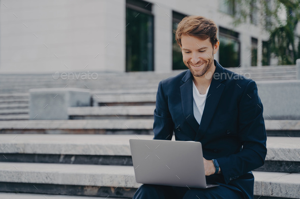 Young businessman sits on steps uses laptop organizes meeting online with investors - Stock Photo - Images