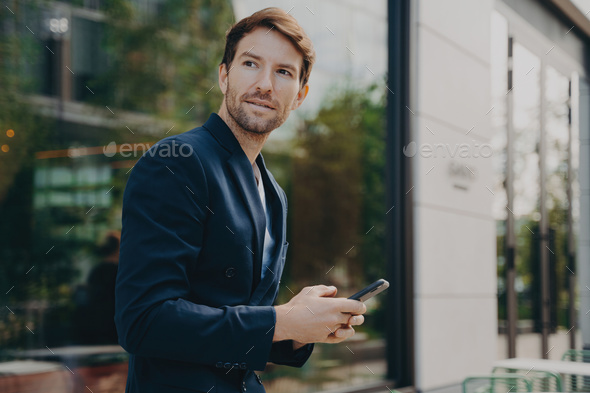 Pensive businessman holds cellular sends text messages dressed formally - Stock Photo - Images