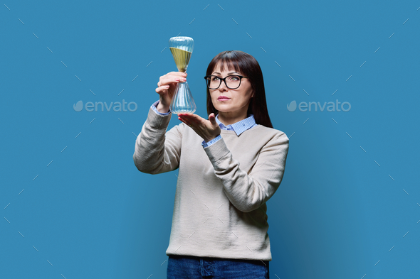 Mature woman holding an hourglass in her hands, on blue background