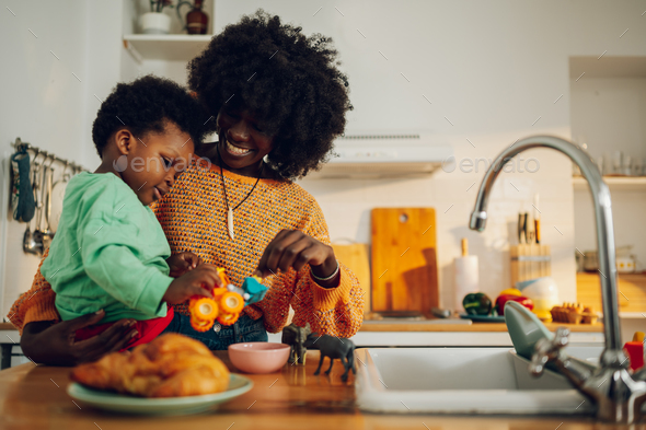 A happy interracial mother and son are playing with toys in the kitchen at home. - Stock Photo - Images