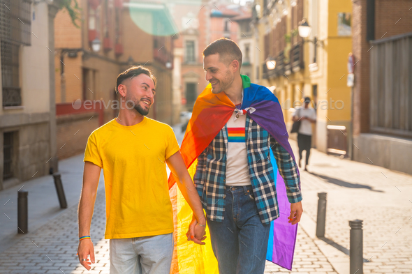 Homosexual men couple walking smiling with rainbow flag at pride party in the city, lgbt concept