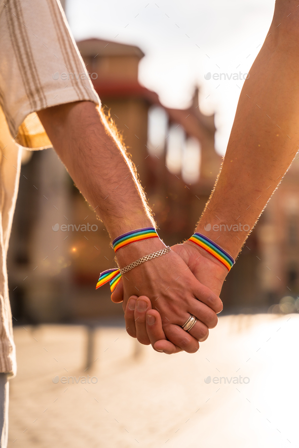 Detail of the holding hands of a couple of homosexual men with the rainbow flag at the pride party