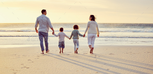 Family with two children holding hands while walking on the beach at ...