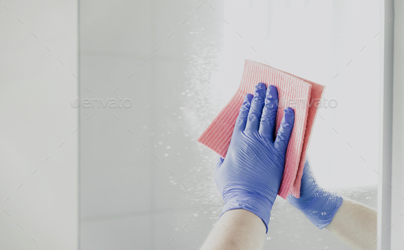Housekeeper woman hand in rubber gloves polishing, cleaning mirror with pink rag - Stock Photo - Images