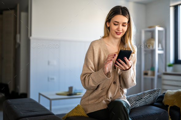 Young woman wearing sweater using smartphone at home, communication and social network concept, - Stock Photo - Images
