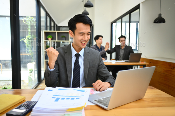 Excited asian male office worker looking at laptop screen, celebrating business success. - Stock Photo - Images