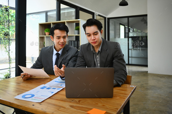Two young businessmen using laptop discussing project strategy at co working office space. - Stock Photo - Images