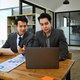 Two young businessmen using laptop discussing project strategy at co working office space. - PhotoDune Item for Sale