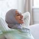Muslim young female student in hijab sitting on sofa at home, hands behind head and resting - PhotoDune Item for Sale