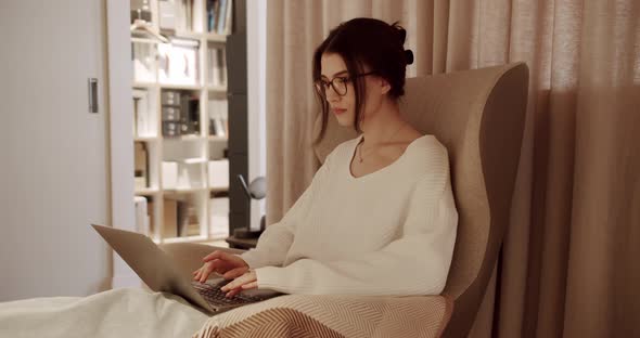 Beautiful Young Woman Works on Laptop Computer While Sitting on the Chair alt