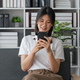 Happy Asian beautiful woman is using mobile phone sitting on a sofa at home - PhotoDune Item for Sale