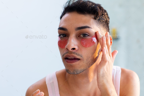 Biracial Transgender Man Looking In Mirror And Applying Under Eye Patches In Bathroom Stock 0305