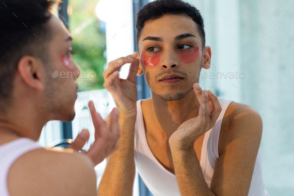 Biracial Transgender Man Looking In Mirror And Applying Under Eye Patches In Bathroom Stock 0218