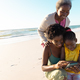 African american senior woman looking at granddaughter and daughter using cellphone at beach - PhotoDune Item for Sale