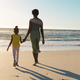 Rear view of african american mother and daughter holding hands and walking towards sea under sky - PhotoDune Item for Sale