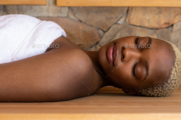 Happy african american woman wearing towel and sitting in sauna