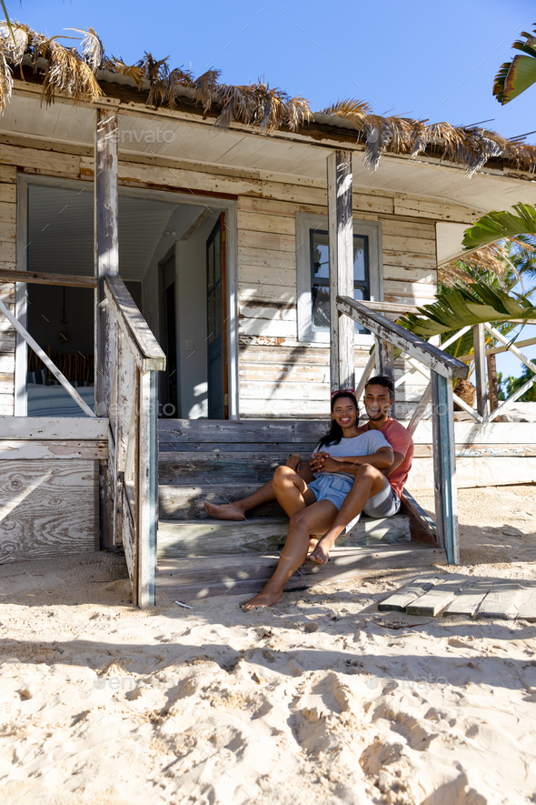 Cheerful caucasian young couple smiling and relaxing on wooden steps outside cottage, copy space - Stock Photo - Images