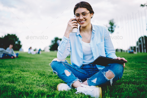 Delighted teen girl sitting in meadow and drawing in sketchbook