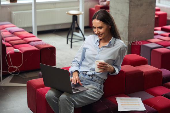 Joyous young woman using her portable computer during coffee break