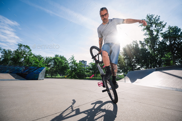 A focused middle-aged professional bmx bike rider is practicing in a skate park for the X games.